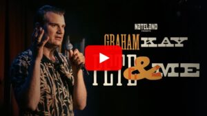 omedian performing stand-up on a club stage with a diverse engaged audience in the foreground