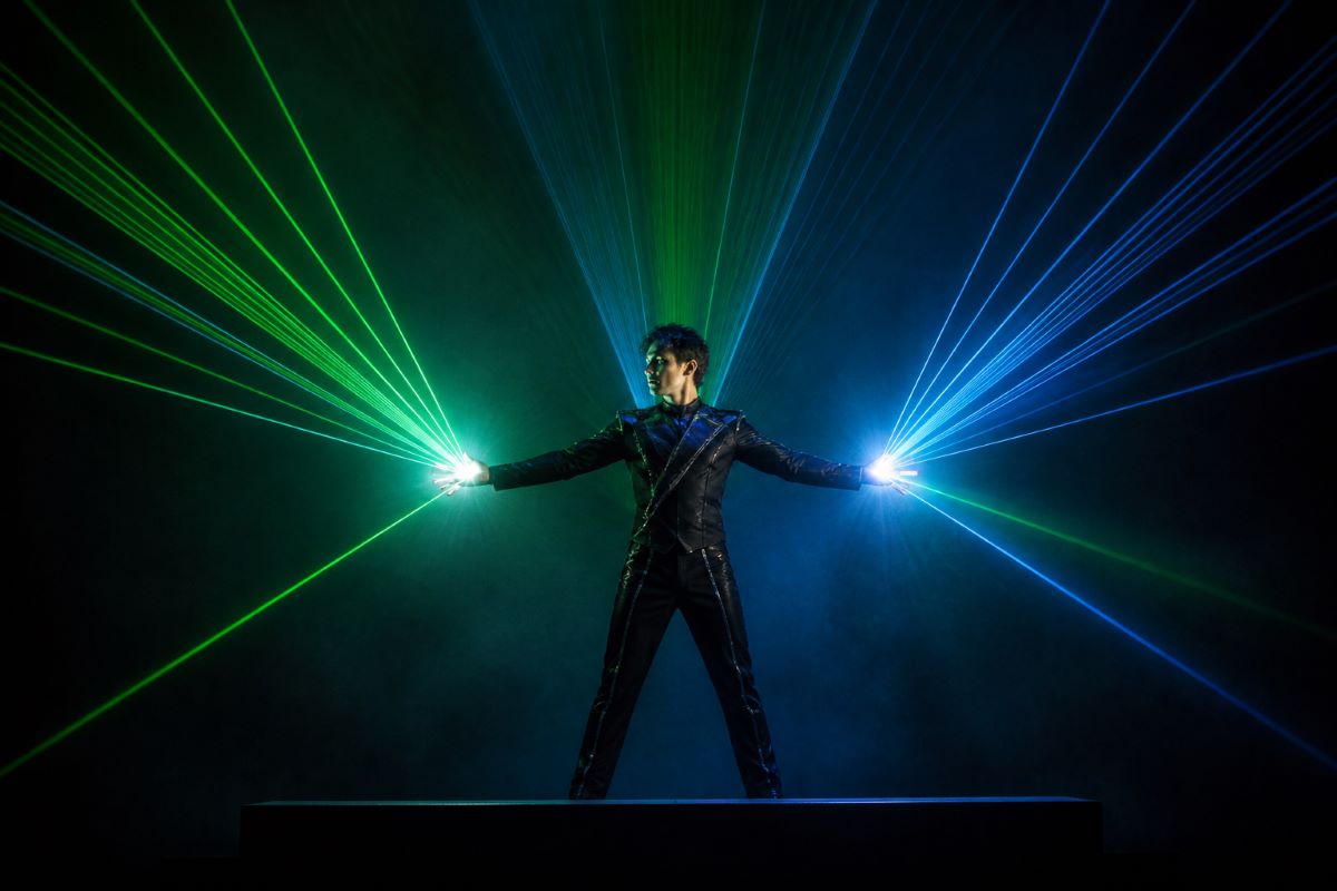 Laser performer bending and manipulating colorful laser beams on a darkened stage