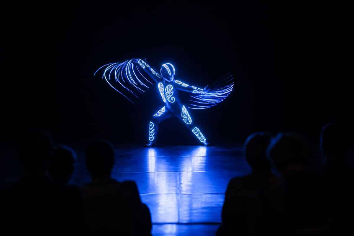 LED dancers in glowing costumes performing on a darkened corporate event stage